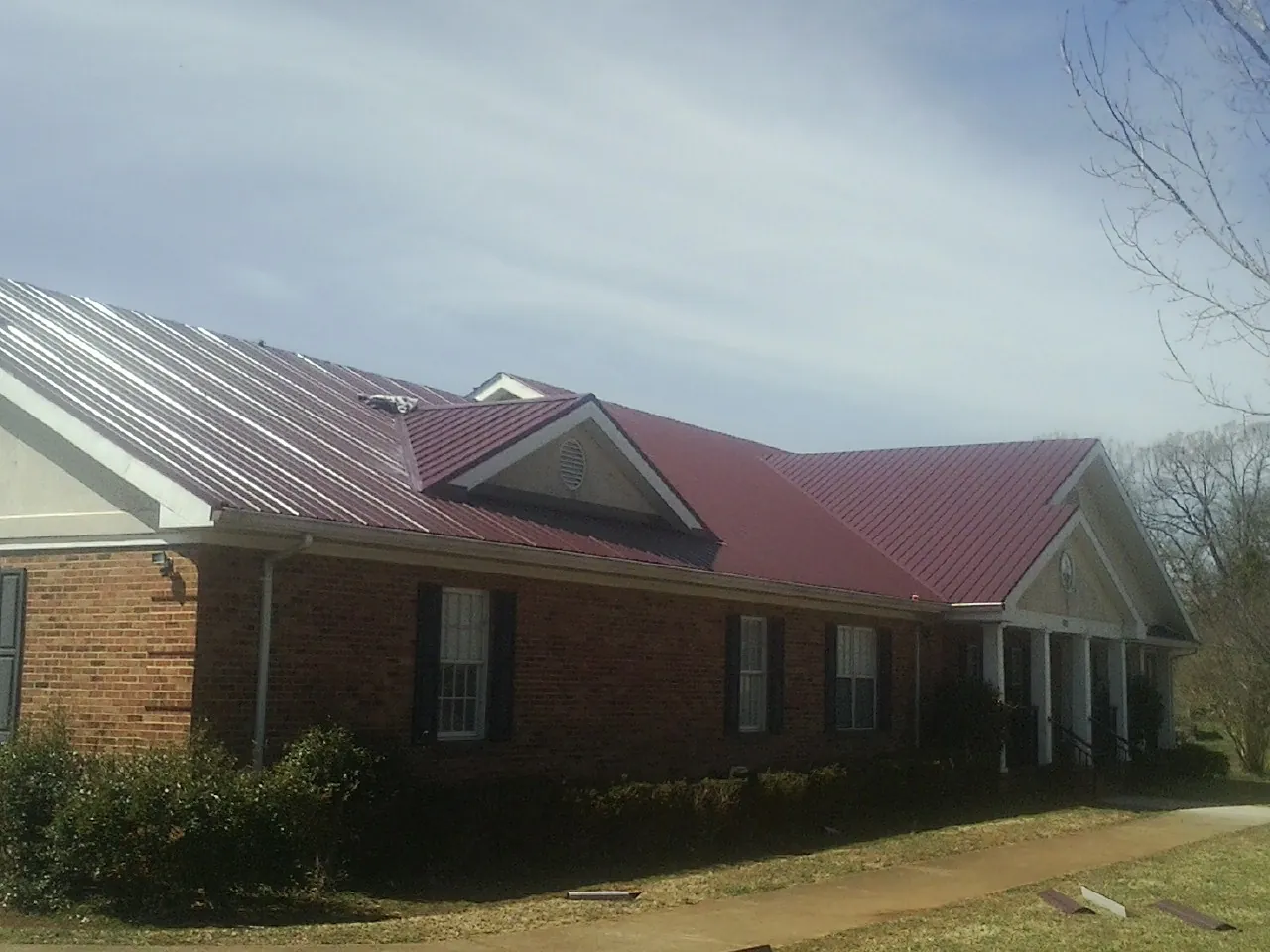 Red metal roof with gabled entries on a long brick building, from a Hail Damage Roof Repair job in Big Cove Tannery