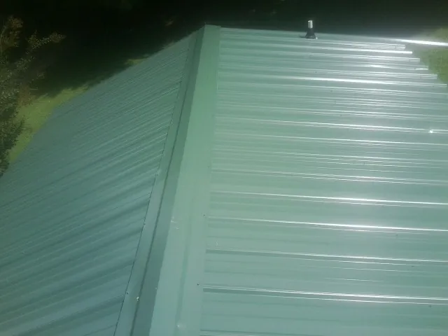 New green metal panels meeting at the ridge of a roof — Flat Roof Repair work by our crew in Big Cove Tannery