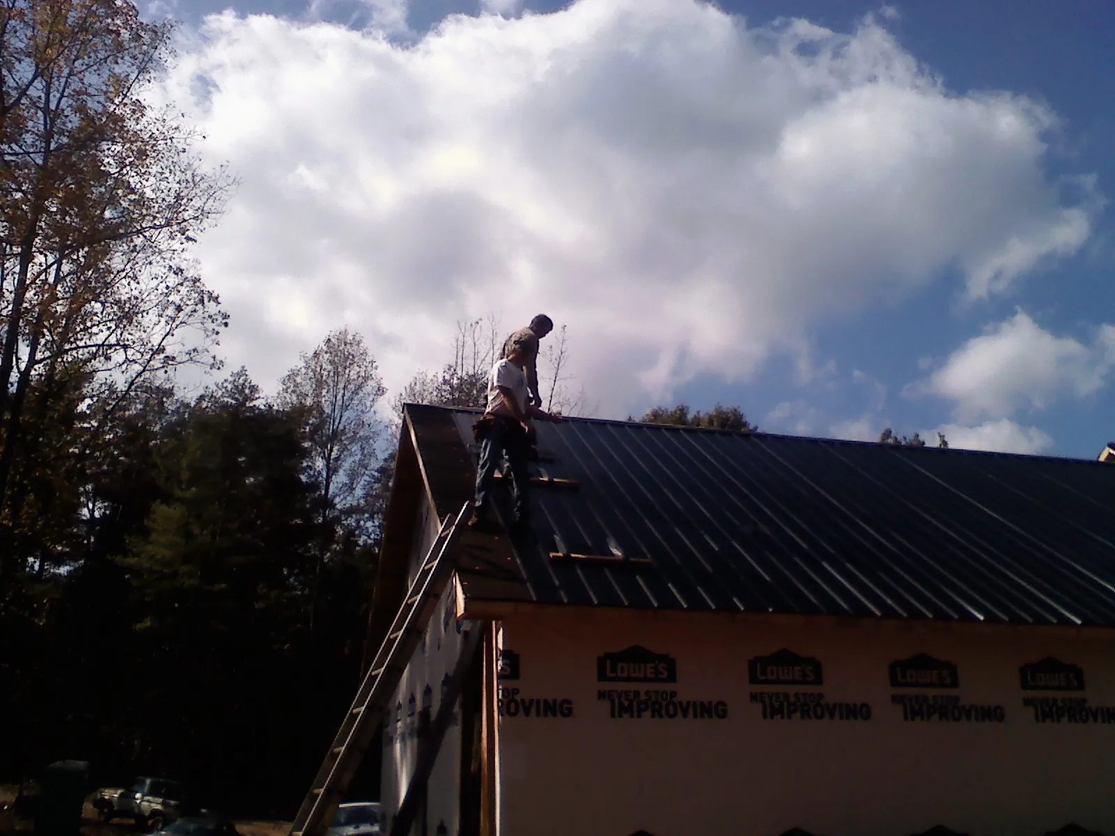 Roofer fastening dark metal panels high against a cloudy sky, from a Roof Inspection job in Big Cove Tannery