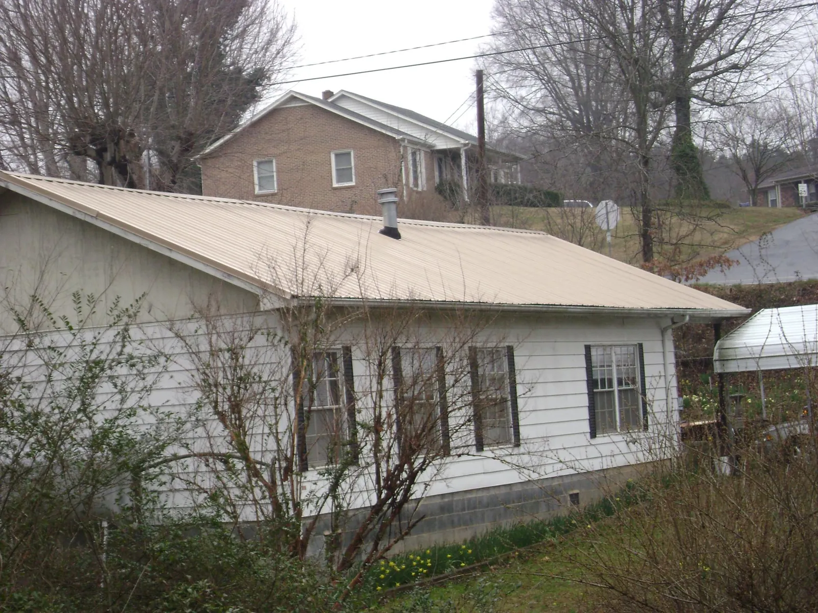 Tan metal roof on a white sided house set into a hillside — Commercial Roofing by Roofing Brothers in Big Cove Tannery
